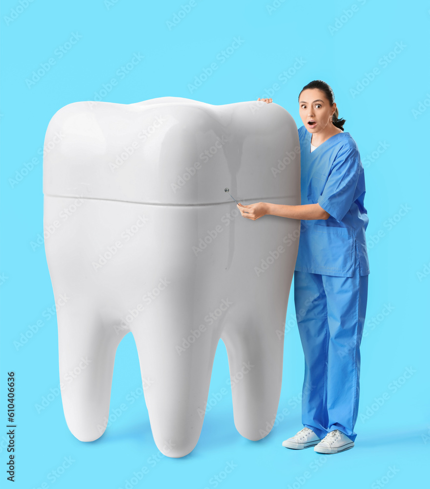 Surprised female dentist with big tooth on light blue background