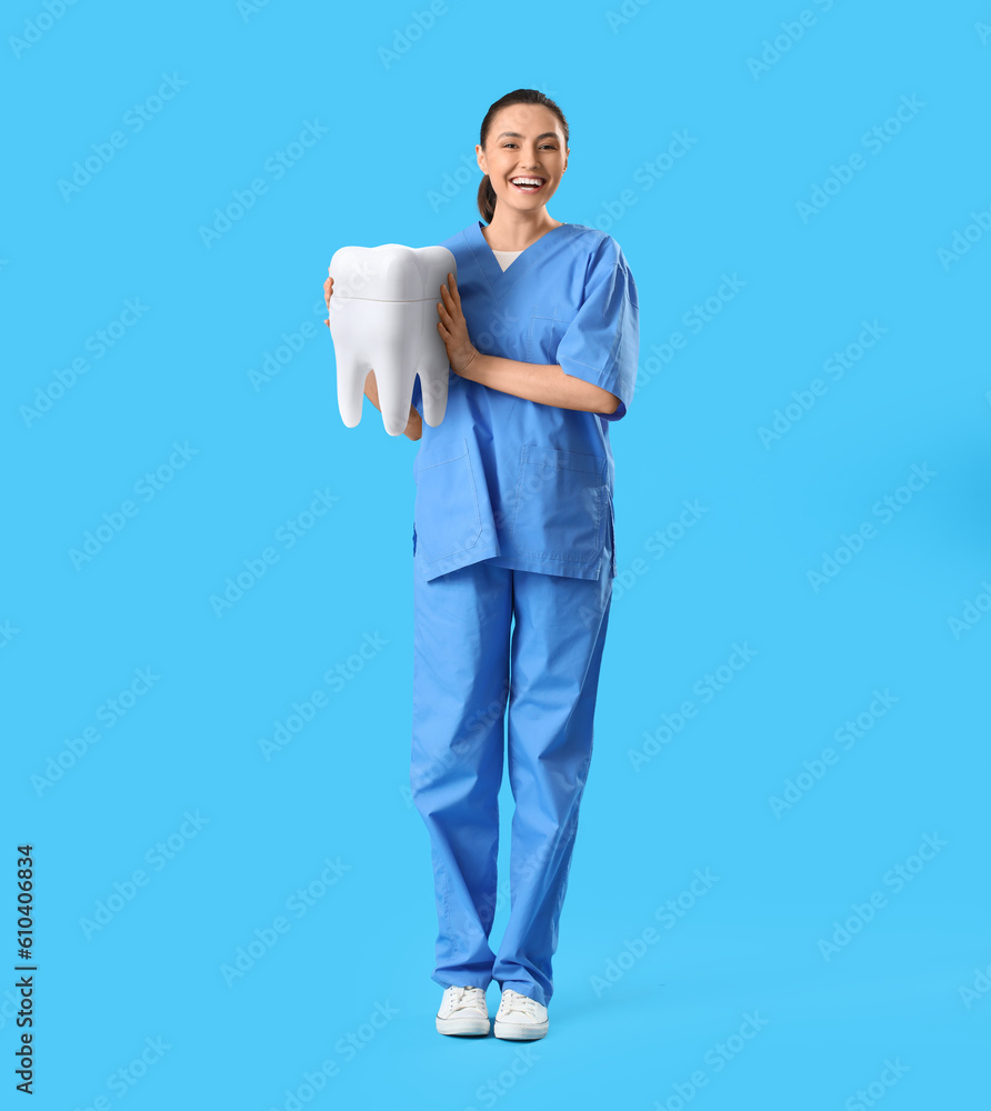 Happy female dentist with big tooth on light blue background