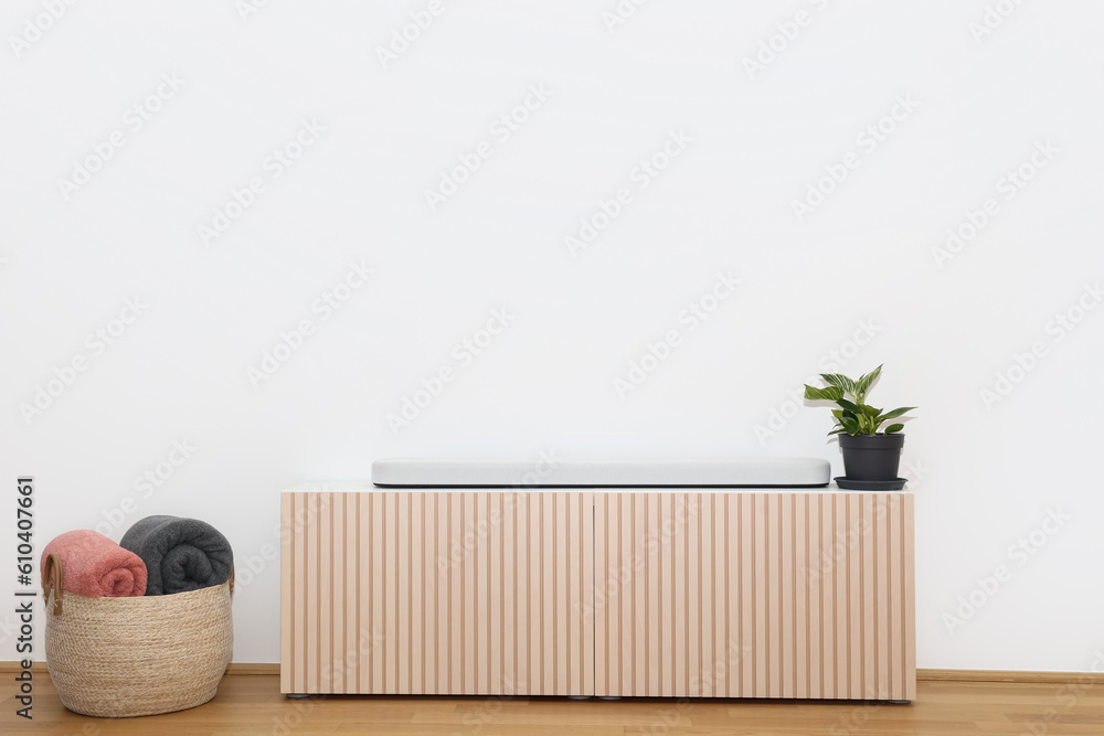 Stylish TV stand, houseplant and basket with plaids near light wall