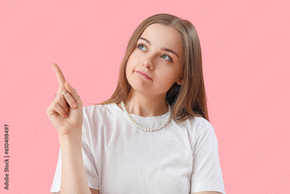 Young woman pointing at something on pink background, closeup