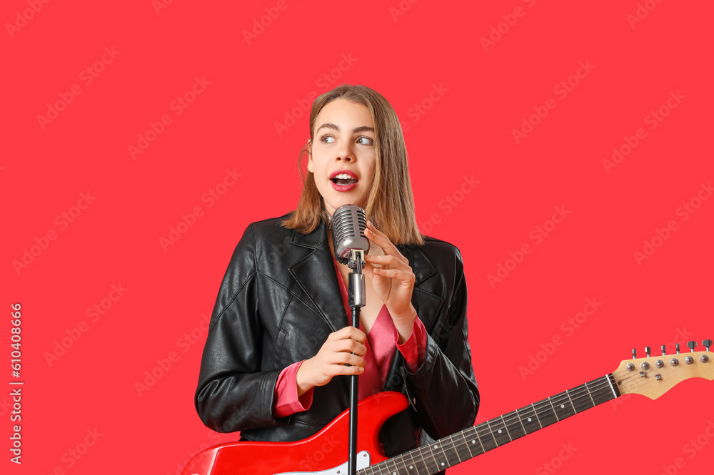 Young woman with guitar and microphone singing on red background