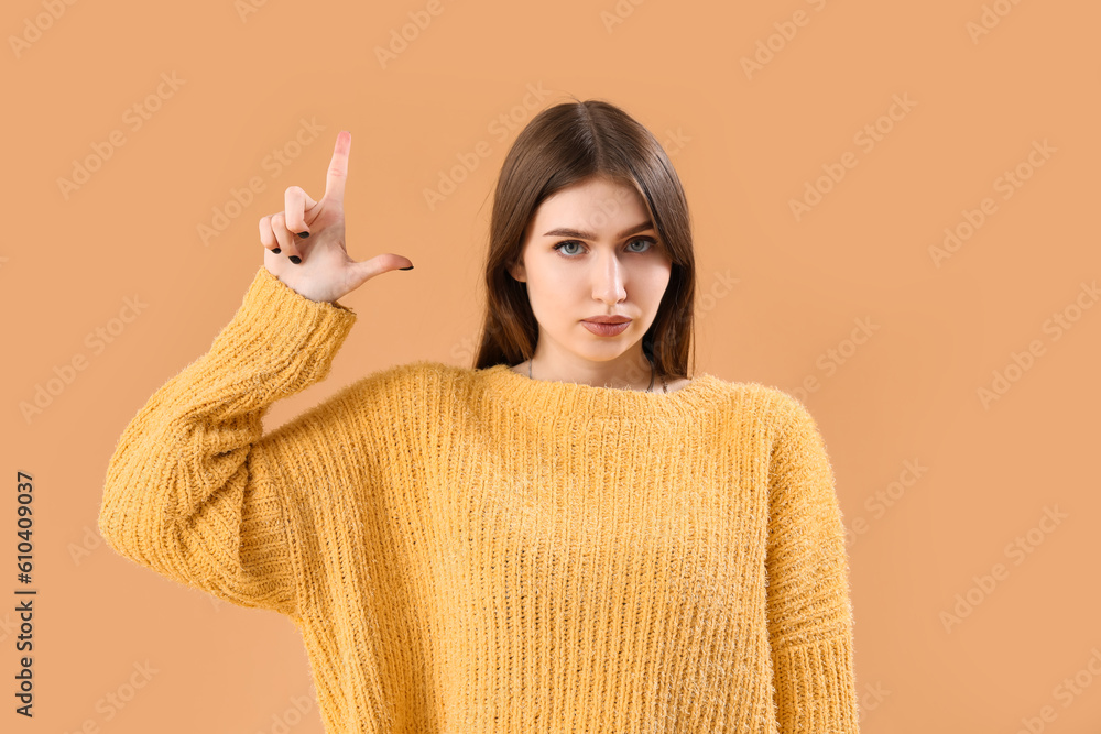 Young woman showing loser gesture on beige background