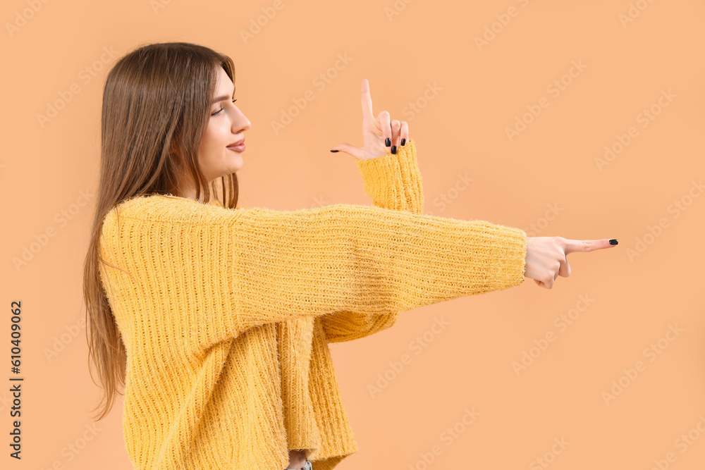 Young woman showing loser gesture and pointing at something on beige background