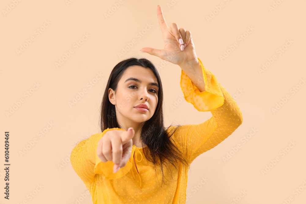 Young woman showing loser gesture on beige background