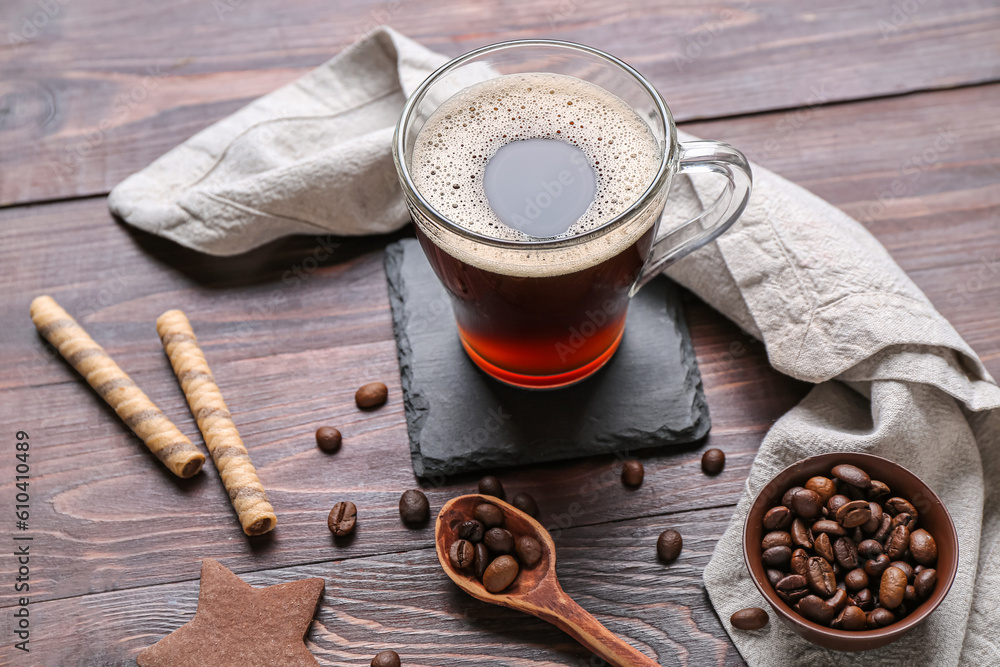 Drink coaster with cup of coffee, wafer rolls and beans on wooden table