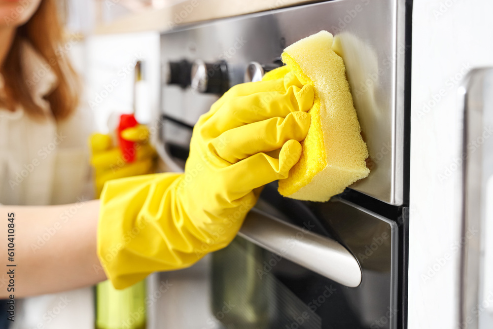 Housewife cleaning electric oven with sponge in kitchen, closeup