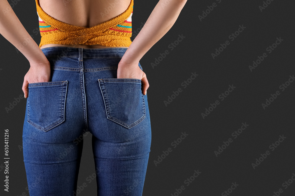 Young woman in skinny jeans on dark background, back view