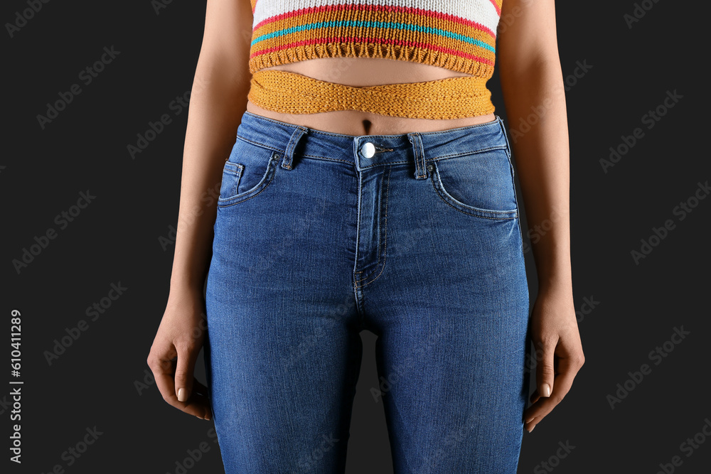 Young woman in skinny jeans on dark background, closeup