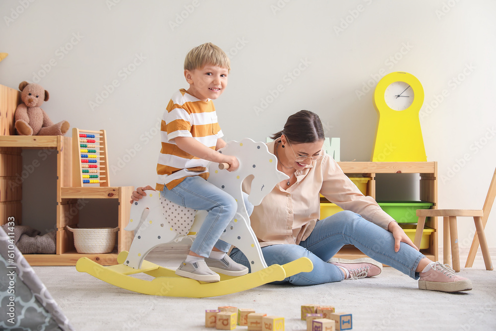 Nanny and little boy playing with rocking horse at home