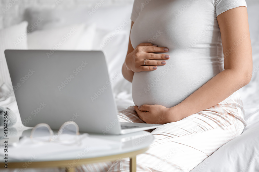 Young pregnant woman working with laptop in bedroom, closeup