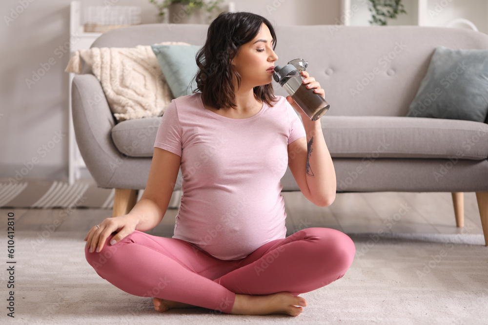 Sporty pregnant woman drinking water at home