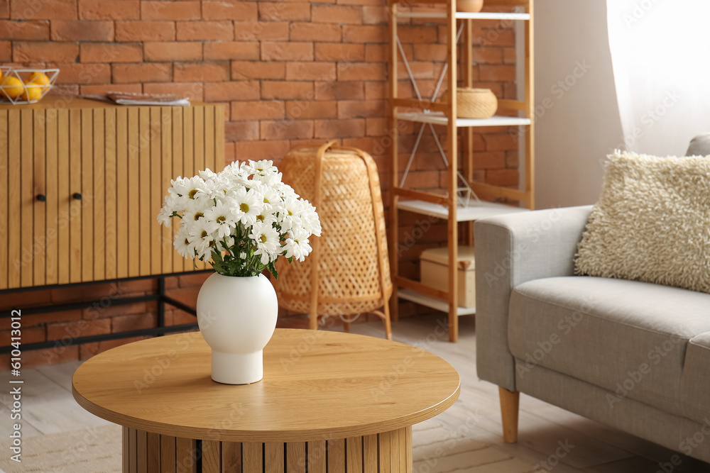 Interior of living room with grey sofa and chrysanthemum flowers on wooden coffee table