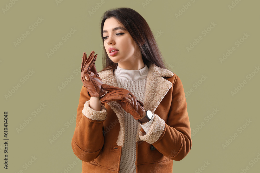 Stylish young woman in leather gloves on green background