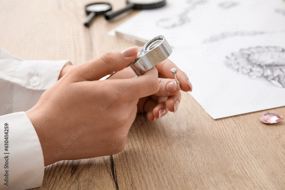 Female jeweler examining ring on wooden table, closeup