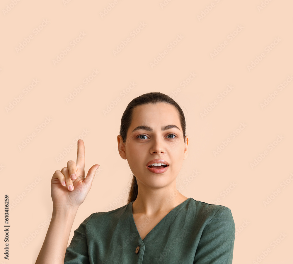 Thoughtful young woman pointing at something on beige background, closeup