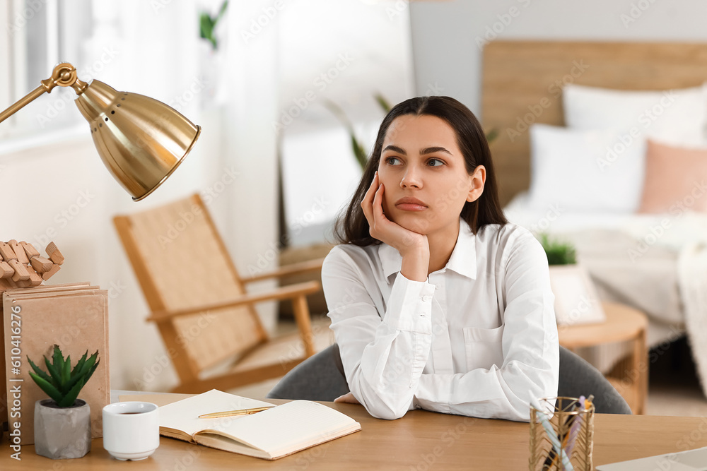 Thoughtful young woman sitting at table in bedroom