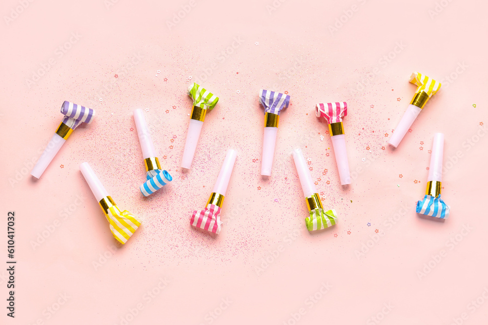 Composition with whistles and sequins for birthday party on pale pink background