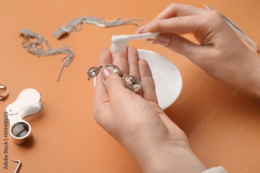 Woman cleaning beautiful earring with toothbrush on color background, closeup