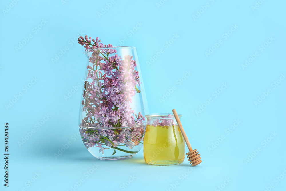 Twig of lilac in glass vase and jar of honey on blue background