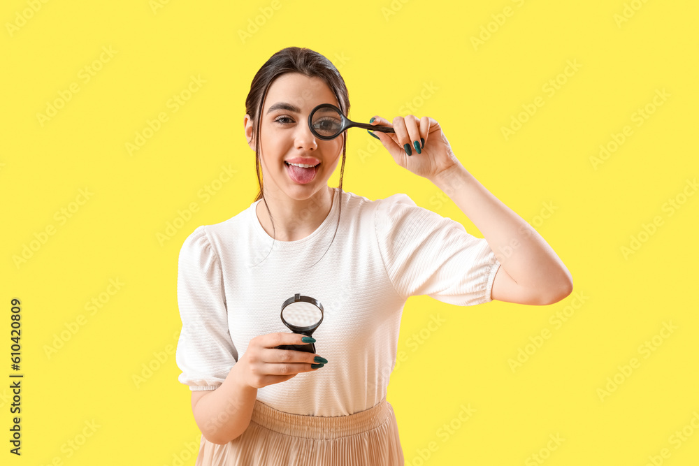 Young woman with magnifiers on yellow background