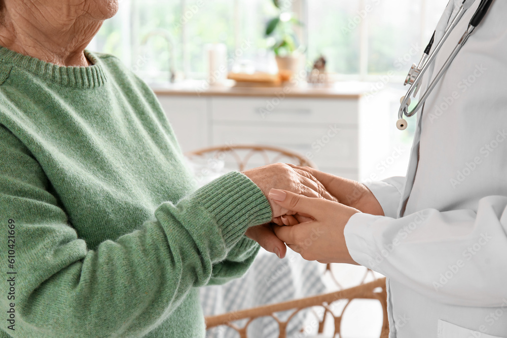 Senior woman with female doctor holding hands at home, closeup