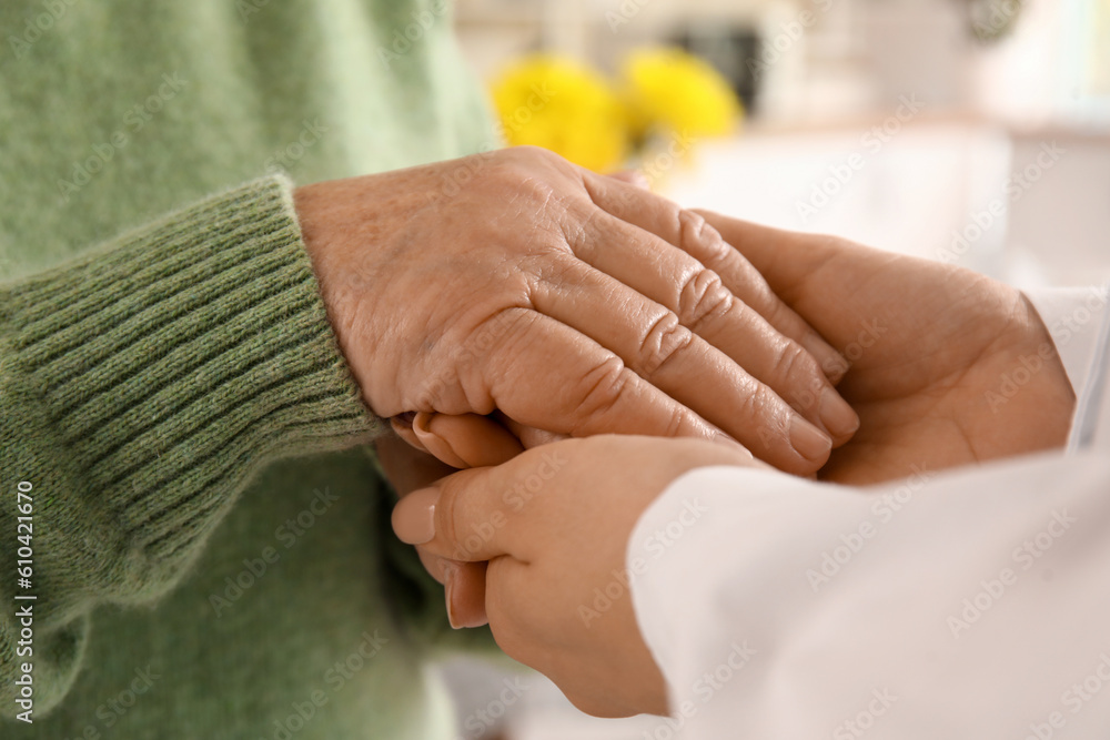 Senior woman with female doctor holding hands at home, closeup