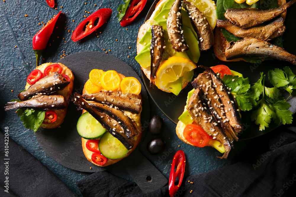 Plate and board of tasty sandwiches with canned smoked sprats on black background