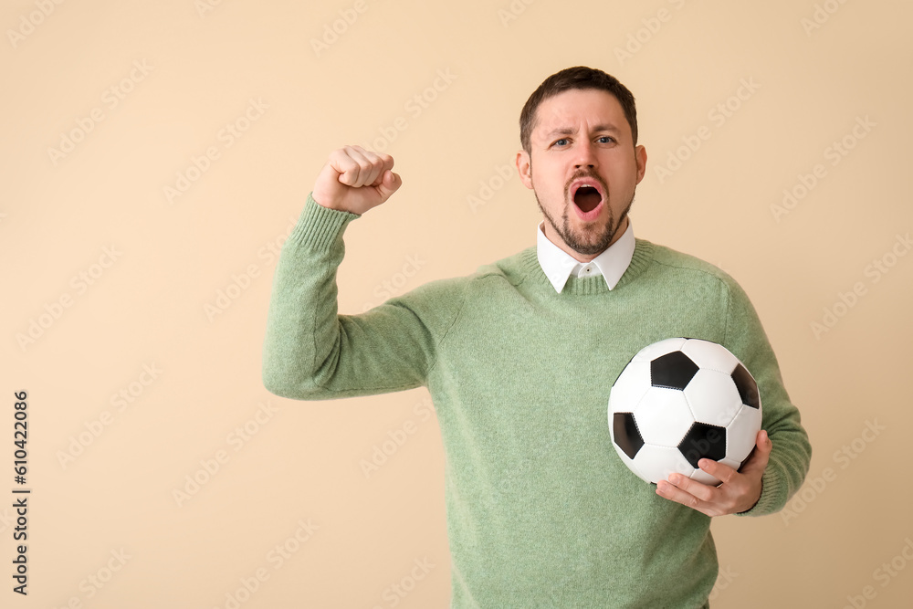 Emotional man with soccer ball on beige background