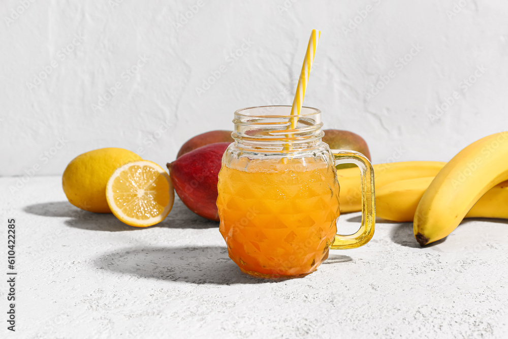 Mason jar of fresh mango smoothie and fruits on light background