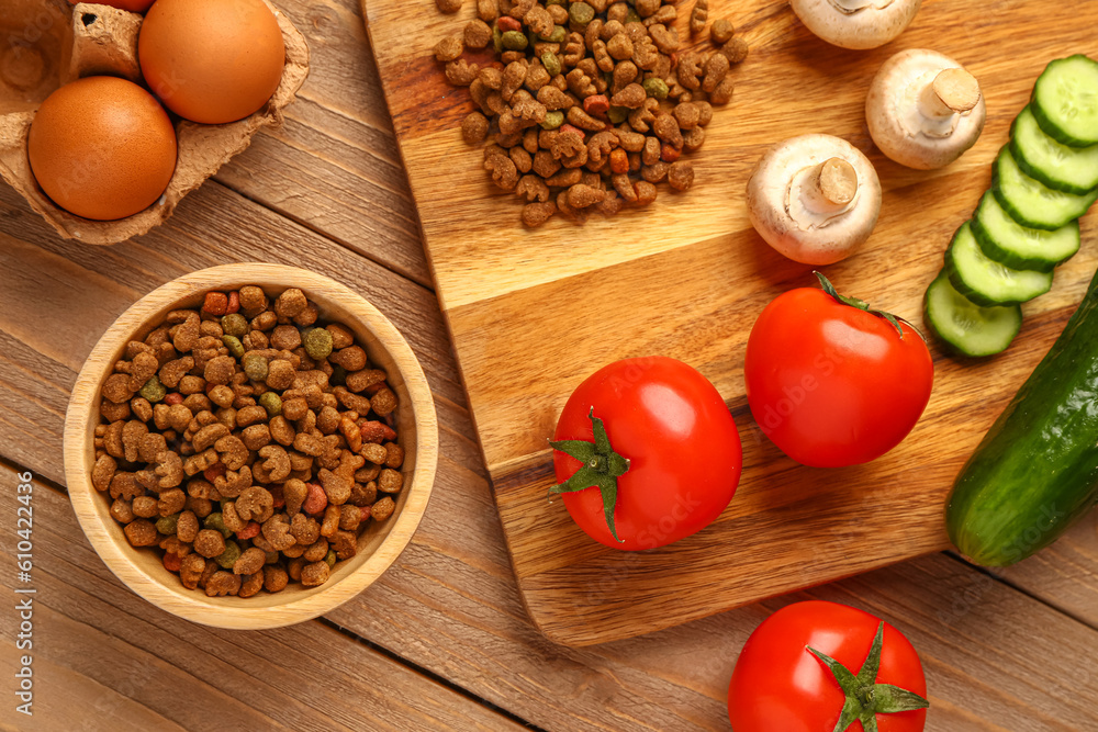 Bowl with dry pet food and natural products on wooden background