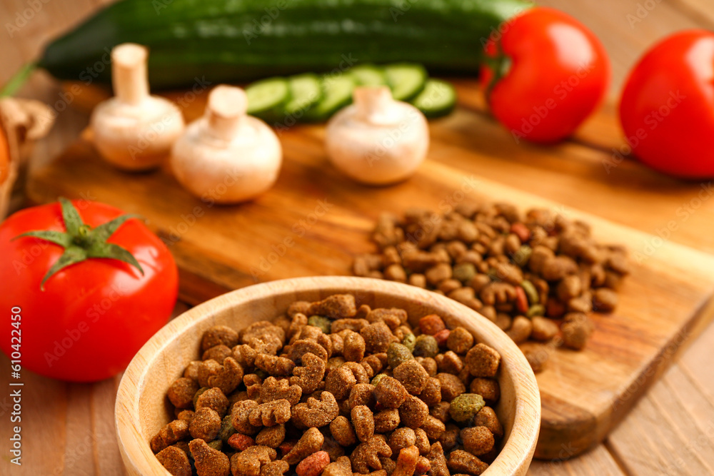 Bowl with dry pet food and natural products on wooden background, closeup