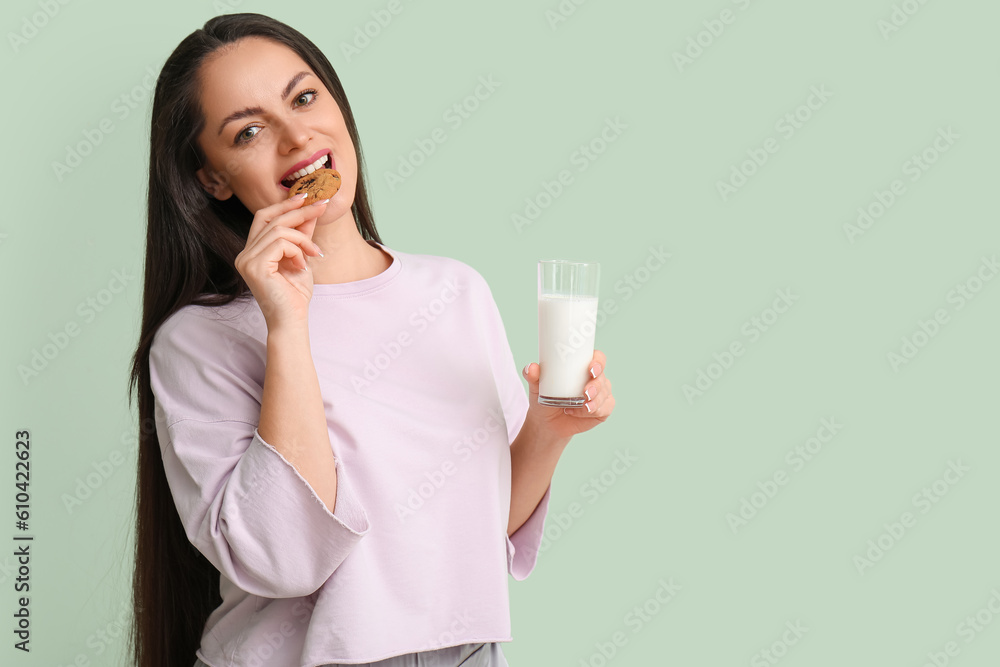 Beautiful young woman with glass of milk and cookie on mint background