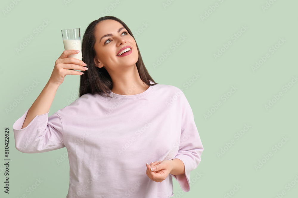 Beautiful young woman with glass of milk on mint background