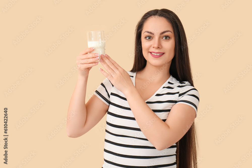 Beautiful young woman with glass of milk on beige background