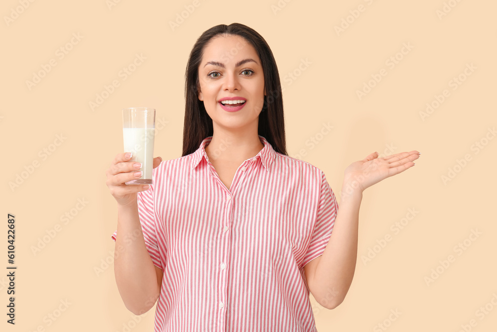 Beautiful young woman with glass of milk on beige background