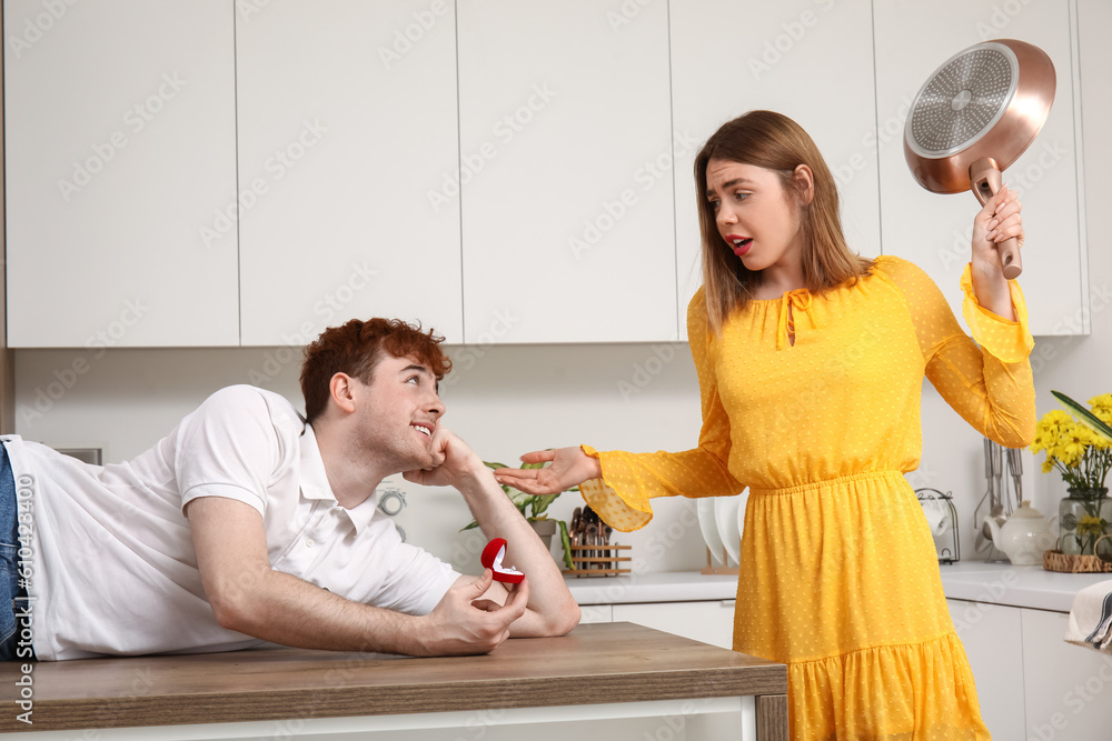 Displeased young woman with frying pan get proposed in kitchen