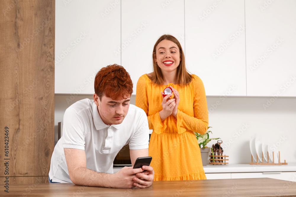 Young woman with engagement ring and her boyfriend using mobile phone in kitchen