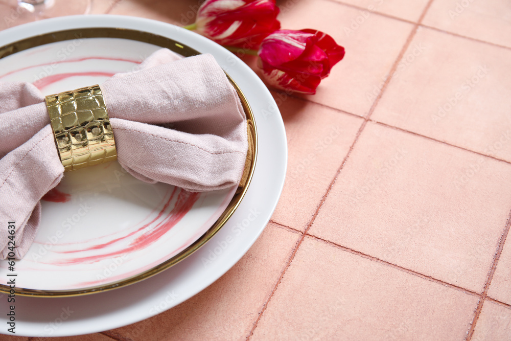 Plates with folded napkin, cutlery and tulip flowers on pink tile background