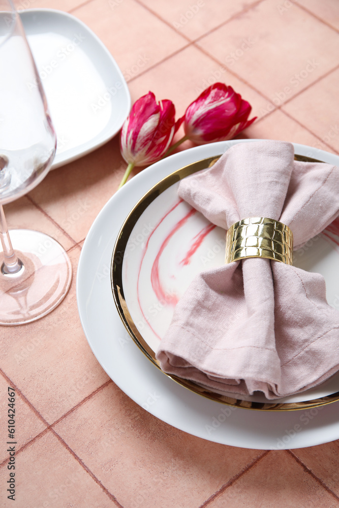 Plates with folded napkin, cutlery and tulip flowers on pink tile background