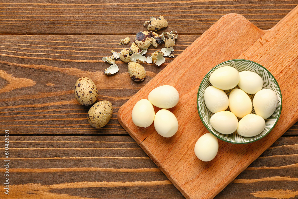 Board with bowl of boiled quail eggs and shells on wooden background