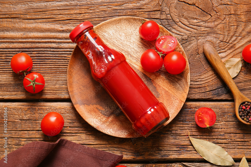 Plate with glass bottle of ketchup and tomatoes on wooden background