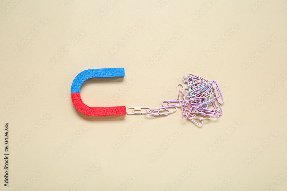 Magnet attracting paper clips on beige background