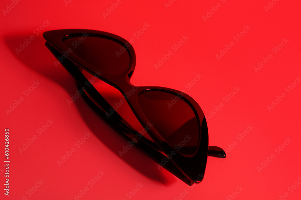 Stylish black sunglasses on red background