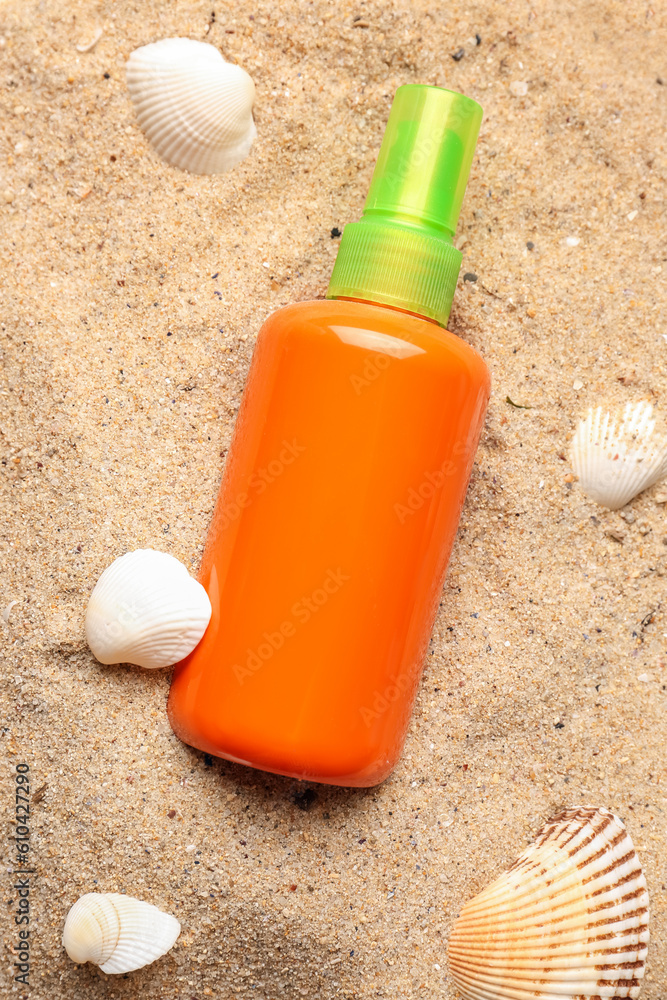 Bottle of sunscreen cream with seashells on sand