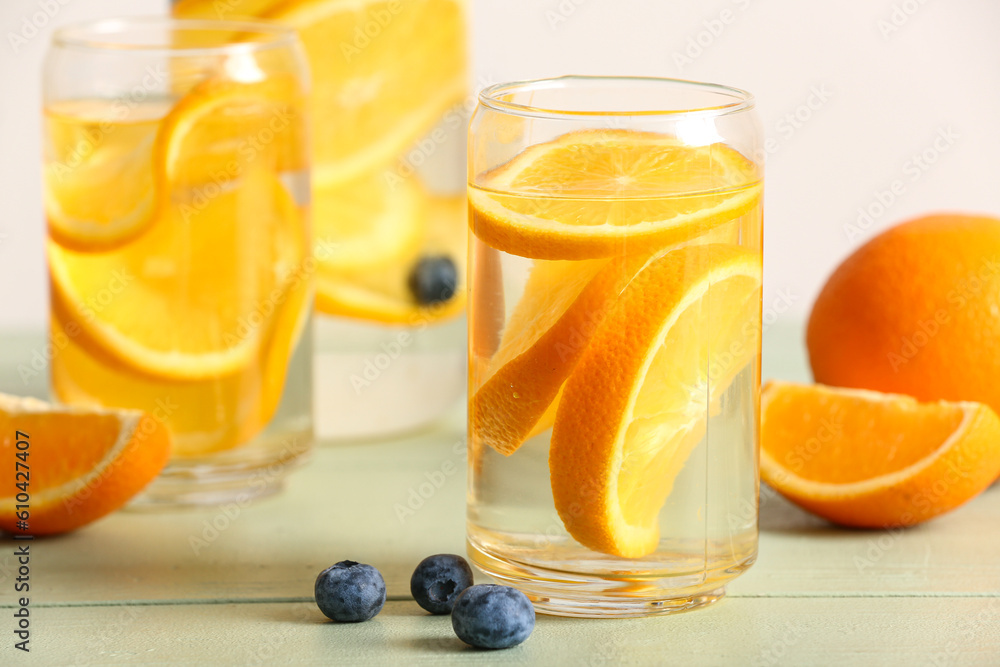 Glasses and bottle of infused water with orange slices on light wooden table