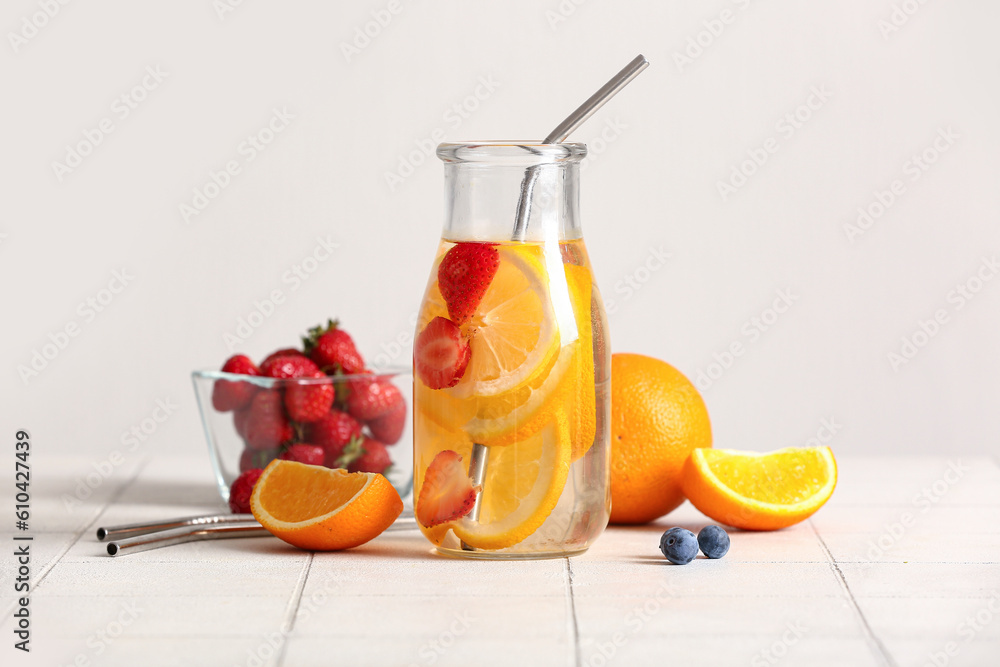 Bottle of infused water with orange slices on white tile table