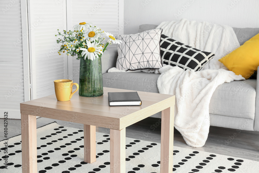 Interior of stylish living room and vase with blooming chamomile flowers on wooden table