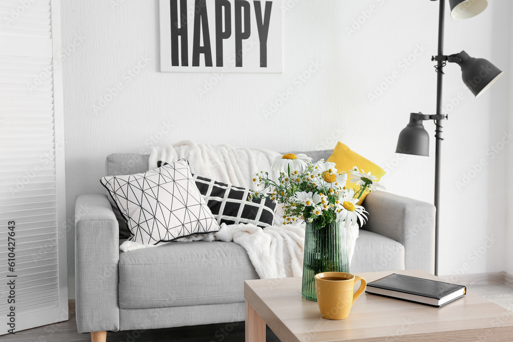 Interior of stylish living room and vase with blooming chamomile flowers on wooden table