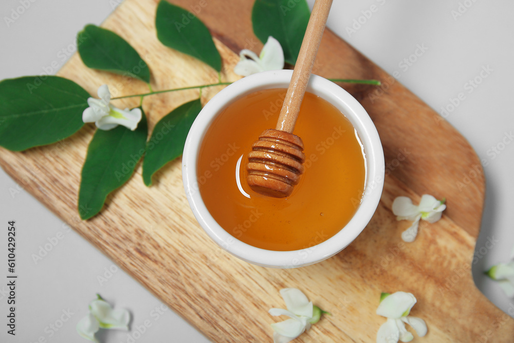 Bowl of honey with flowers of acacia and branch on white background, closeup