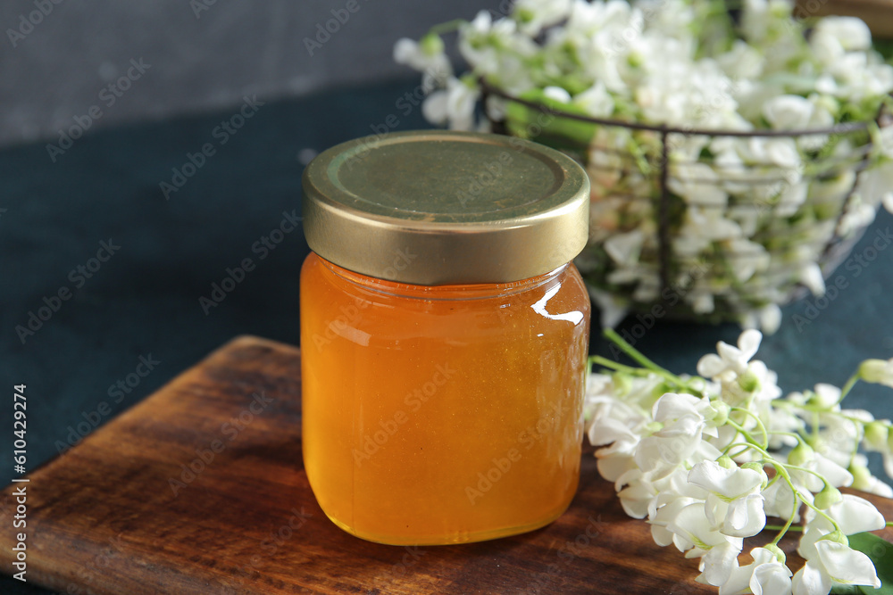 Jar of honey with flowers of acacia on dark background, closeup